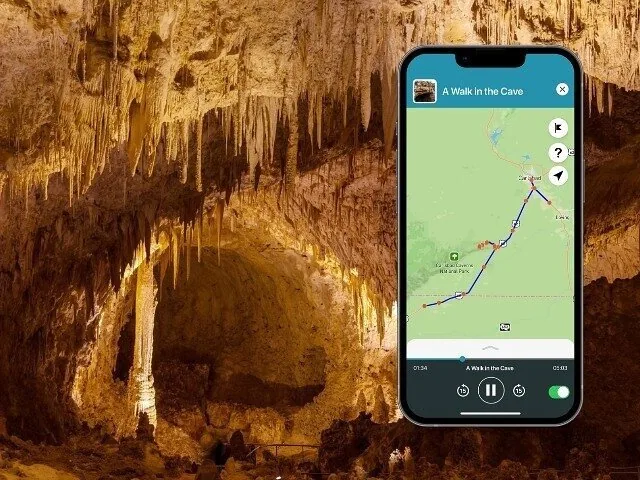 An illuminated cave interior with a smartphone displaying an audio tour app interface.